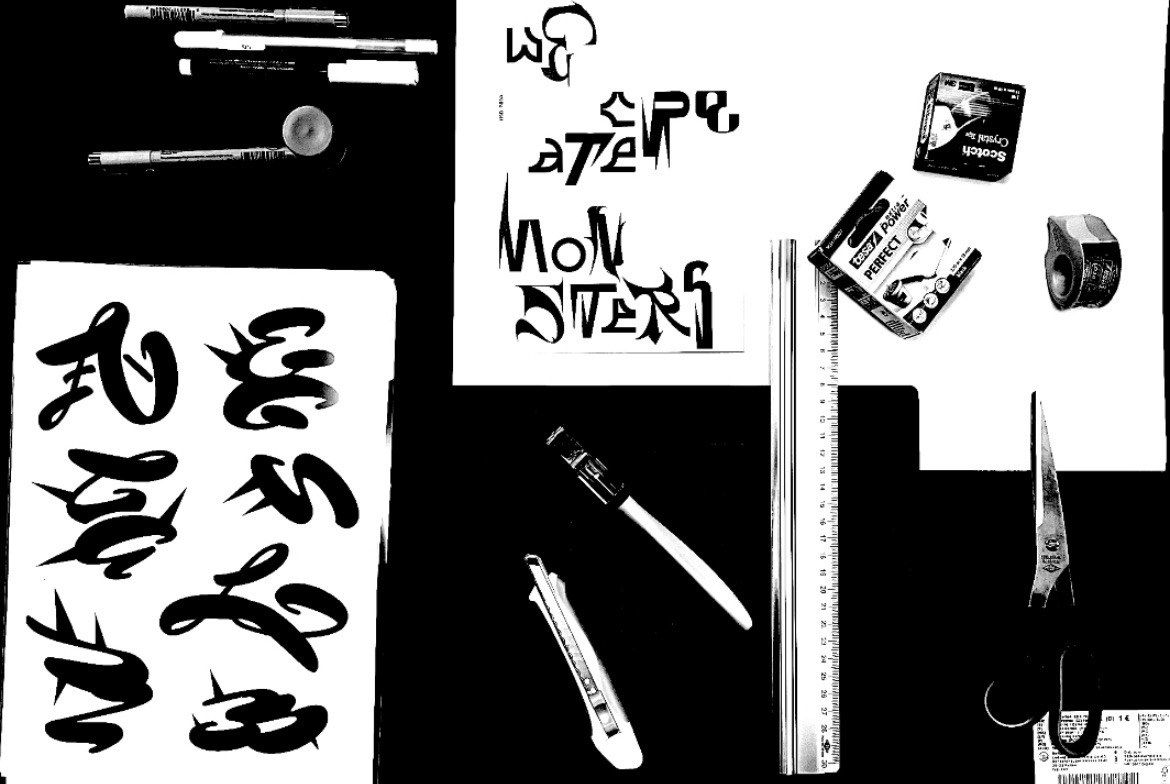 Cut letterforms, drawing tools, tape, and rulers arranged on a black-and-white worktable