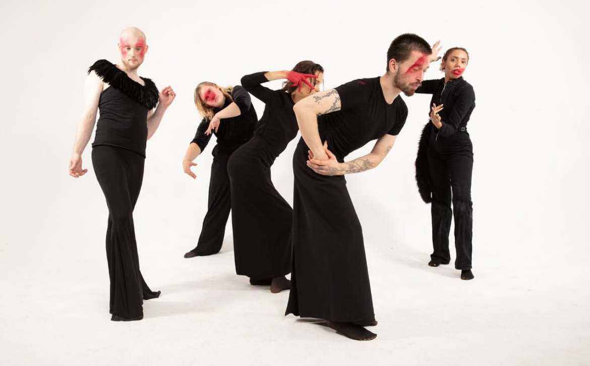 Five performers in black and red makeup holding sculptural poses