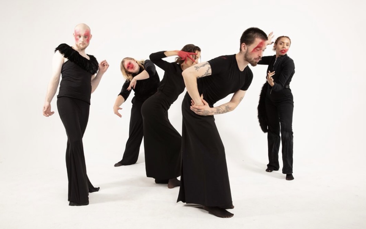 Five performers in black and red makeup arranged in a dynamic formation