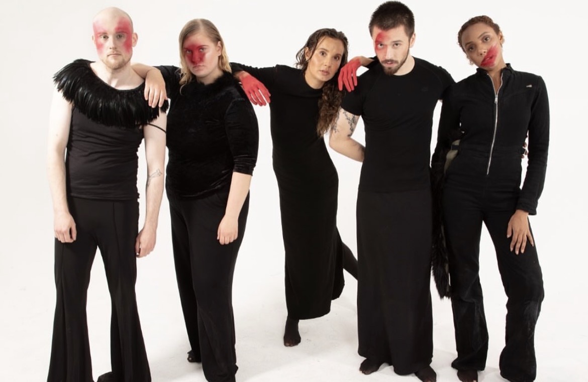 Five performers standing shoulder to shoulder in black and red makeup