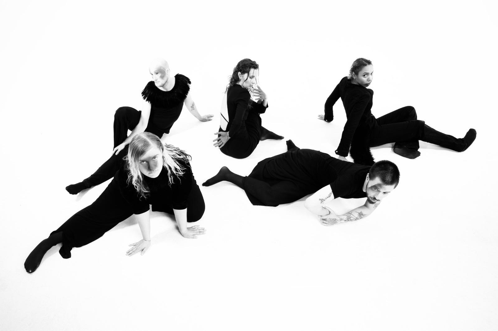 Five performers spread across the white studio floor in a sculptural arrangement