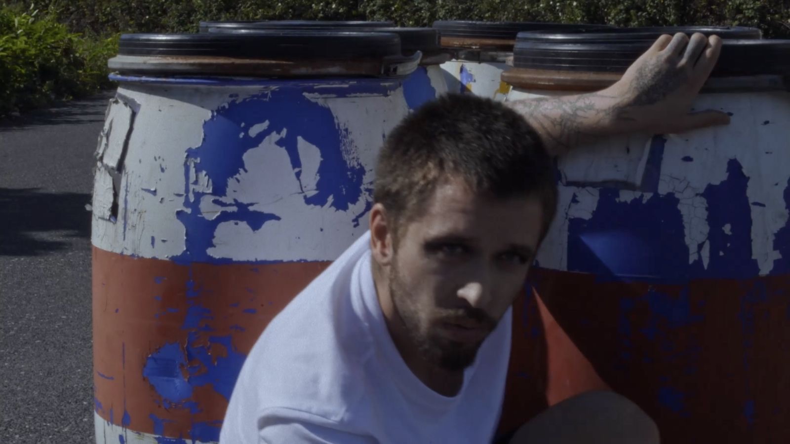 Performer seated against painted industrial barrels