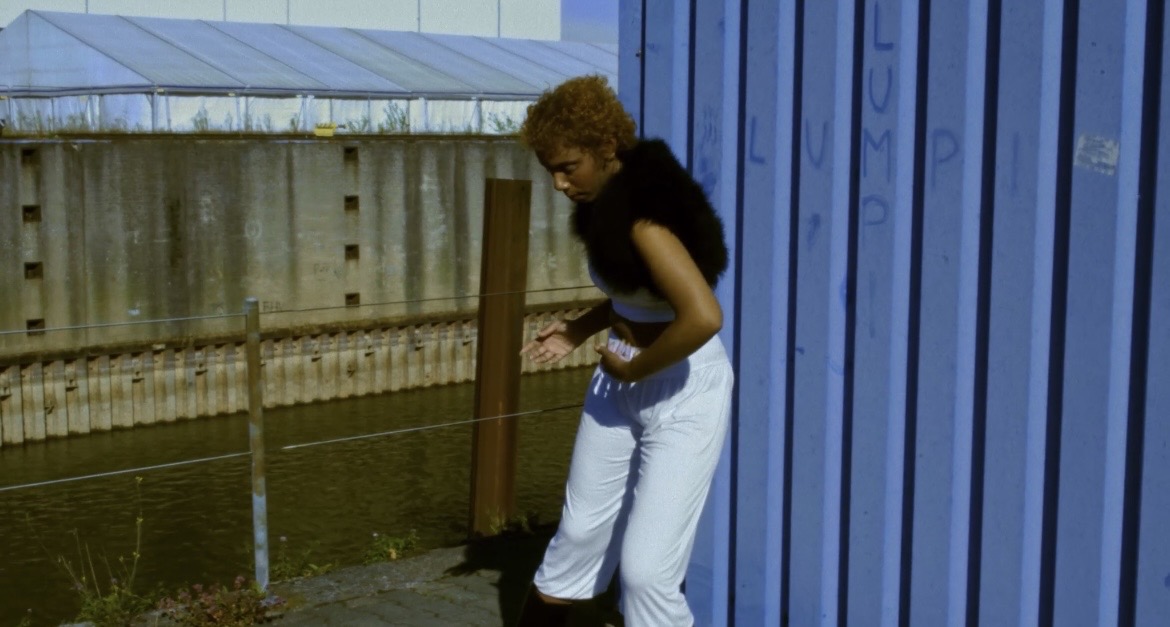 Performer beginning a gesture beside a blue industrial structure