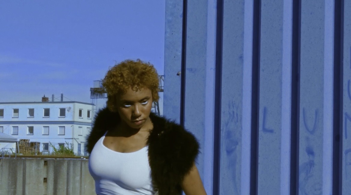 Portrait of the performer standing beside blue industrial architecture