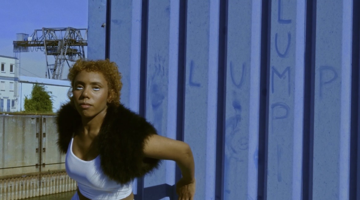 Performer leaning into a movement beside the blue wall