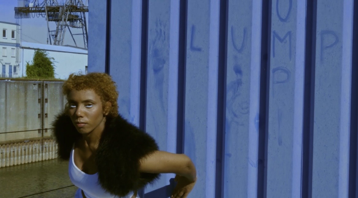 Performer holding a low pose beside the blue wall and water